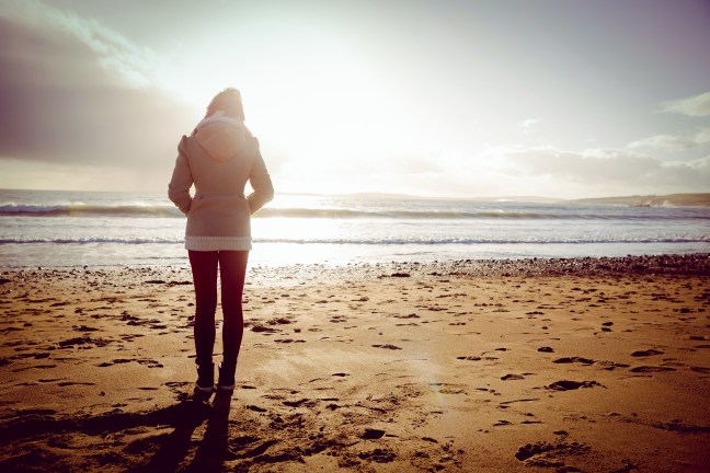 Rear view of woman looking at the sea during the sunset on the beach in front of camera